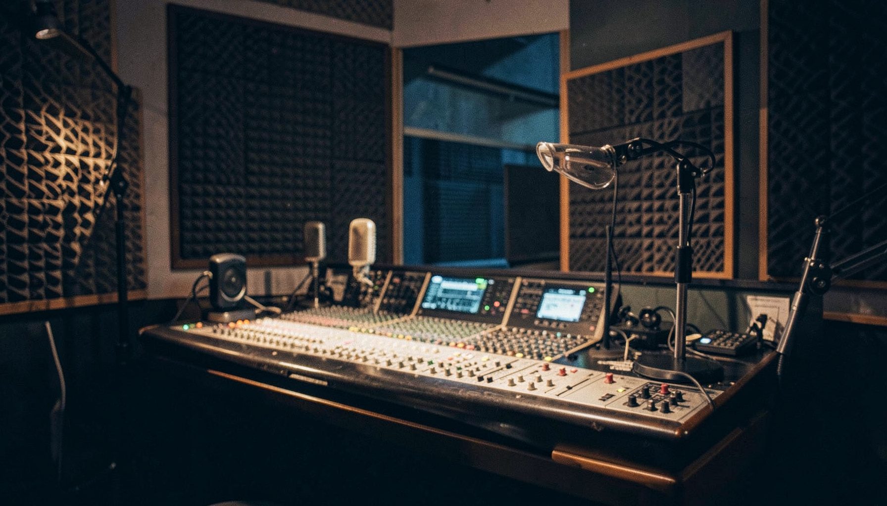 A warm, dimly lit radio studio with vintage microphones, a mixing console, and acoustic foam panels; deep amber and charcoal tones dominate the scene.